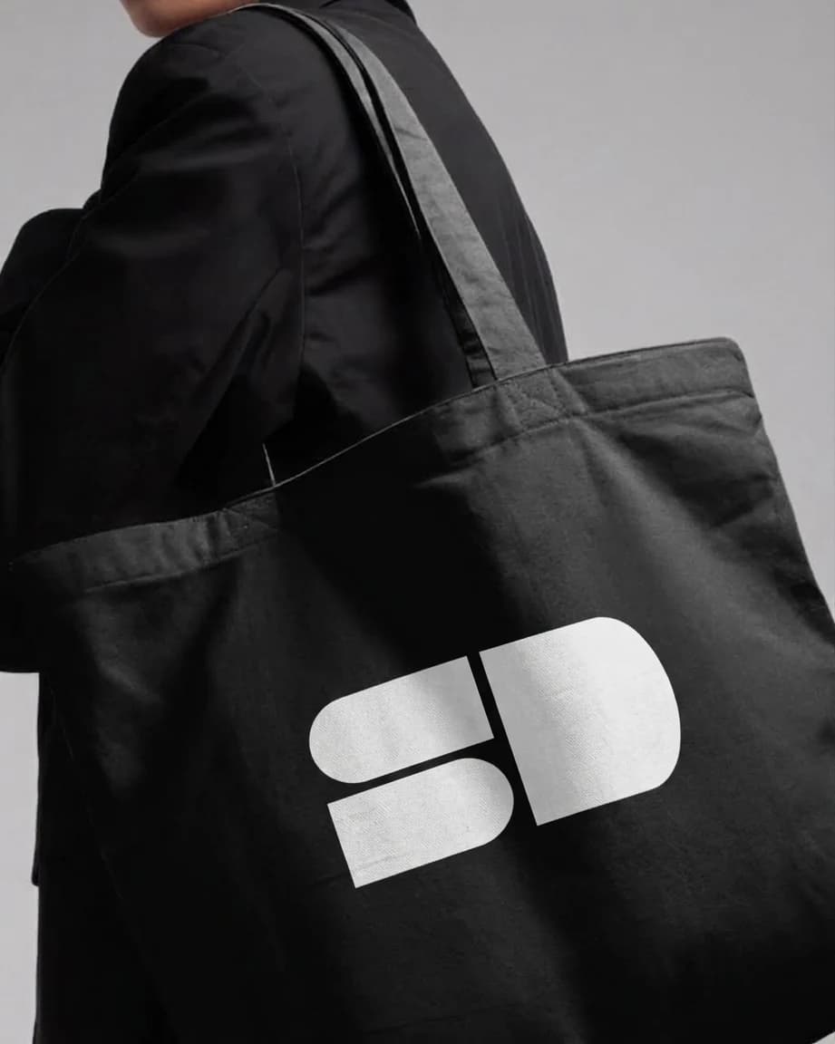 Pessoa com uma bolsa preta estampada com a marca Same Different em branco.